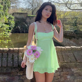 Woman in a light green dress holding flowers outdoors near a brick wall and pond.